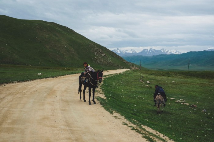 Two children on horses by a track leading through the hills