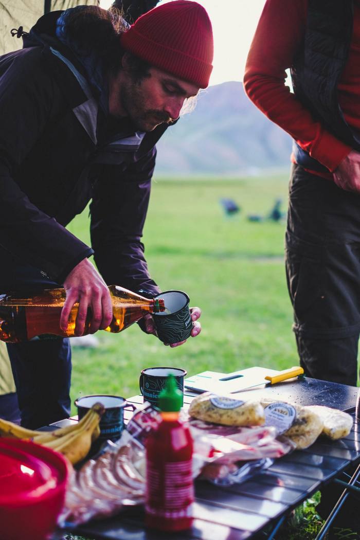 A man leans over a table where food is set out, he pours a cold drink